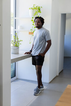 Man leaning against concrete counter by tall window in flat, smiling and checking watch with plant
