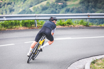 Obraz premium Young caucasian man going downhill on a corner with a road bike on an asphalt road of a mountain.