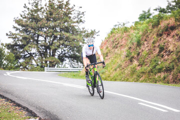 Fototapeta premium Young caucasian woman going downhill on a corner with a road bike on an asphalt road of a mountain.