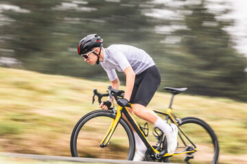 Obraz premium Young caucasian man riding a bike climbing a hill