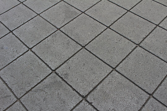 Texture of square paving tile. Grey sidewalk tiles in the street. Concrete pavers close up background.