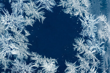 Macro photo of delicate ice and hoarfrost crystals forming natural snowflake patterns on a deep blue winter background, ideal for seasonal, cold, and abstract concepts.