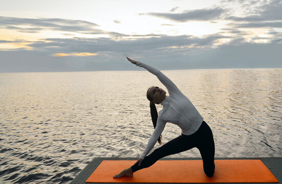 Parighasana background of sunset sky, silhouette of woman in sports clothes hatha yoga lovers practicing oriental system of exercises Woman performs parighasana gate pose Ada Ciganlija Belgrade