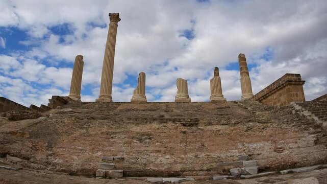 Uthina archaeological site in Tunisia featuring ancient Roman columns on elevated terrace, wide angle view overlooking countryside beneath dramatic cloudy sky, highlighting classical heritage