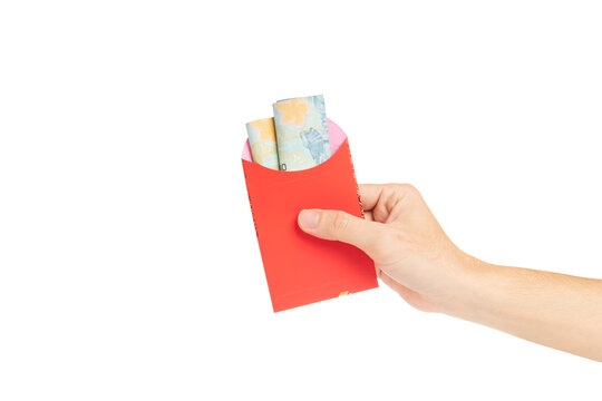 Close up of hand holding a red envelope or angpao filled with Indonesian Rupiah banknotes, isolated on white background.