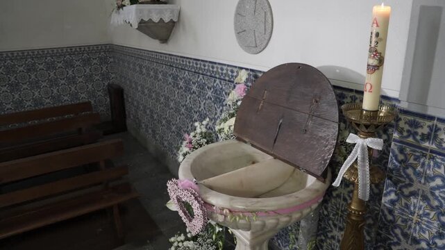 Baptismal font with open wooden lid candle floral decoration and tile walls