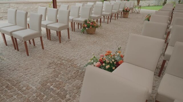 Rows of white chairs arranged for outdoor wedding ceremony with floral aisle accents