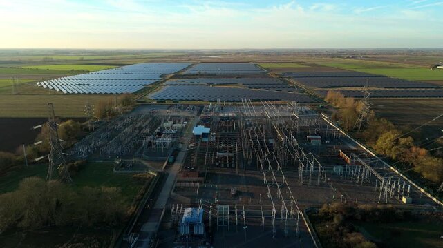 Drone flight over vast photovoltaic solar panel array and high voltage electrical power station in Burwell UK supporting British grid upgrades
