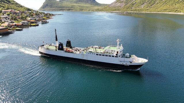 14 july 2025, Gryllefjord, Norway. Aerial, bird view, above the water of a fjord, Ferry from Gryllefjord toward Andenes on Lofoten left the harbor, turning in fjord. Village visible, mountains. Travel
