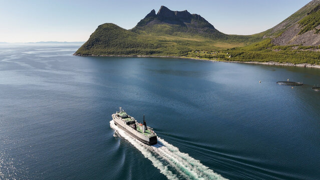 14 july 2025, Gryllefjord, Norway. Aerial, bird view, above the water of a fjord, Ferry from Gryllefjord toward Andenes on Lofoten left the harbor, in fjord. Village visible, mountains. Travelling by 