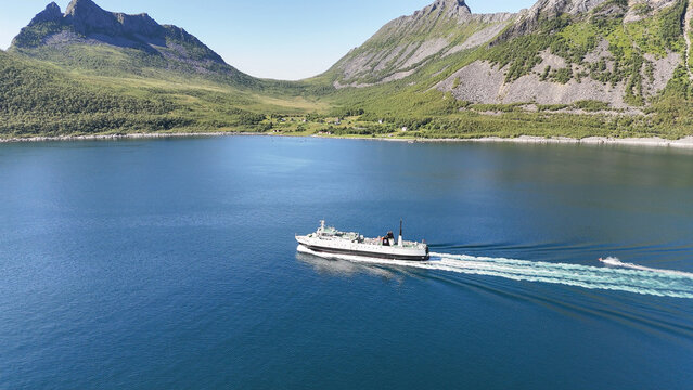 14 july 2025, Gryllefjord, Norway. Aerial, bird view, above the water of a fjord, Ferry from Gryllefjord toward Andenes on Lofoten left the harbor, in fjord. Village visible, mountains. Travelling by 