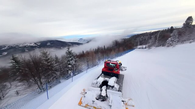 Dynamic FPV drone chase following a snow groomer on a ski slope. Fast aerial footage of a snowcat machine working on the Jaworzyna peak in Szczyrk, Poland, surrounded by a winter mountain landscape.