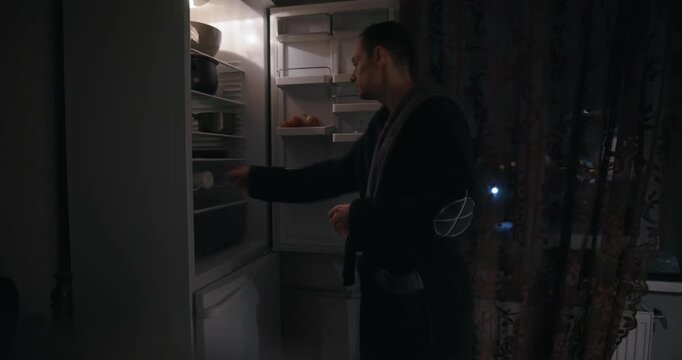 A man opens the refrigerator at night and drinks kefir