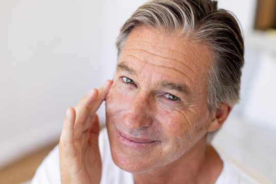 Mature man touching cheek with fingertips while seated at home wearing white T-shirt