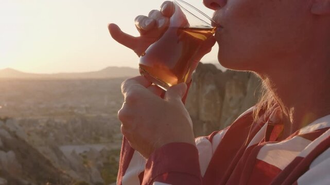 Woman enjoys drinking Turkish tea at sunset in mountain valley in Cappadocia close-up