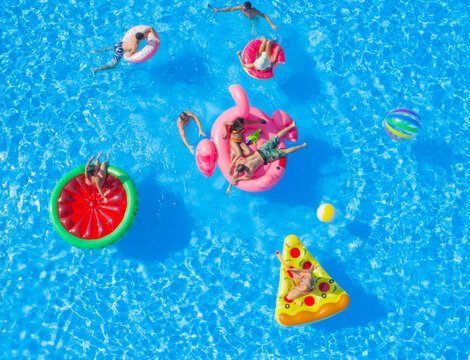 AERIAL: Cheerful young friends having a watergun fight on floaties at pool party