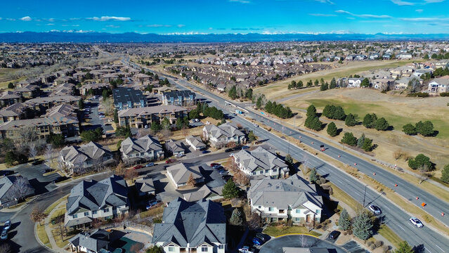 Roadway near E 470 shows active lane work by neighborhoods leading toward wide open greenspace. Bright cones, mixed shingles, pale winter vegetation shape transitional suburban view, Aurora, CO