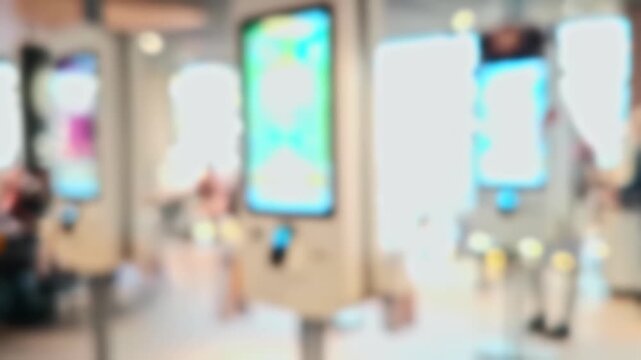 Unfocused video of a modern fast-food interior. People order from digital kiosks with glowing menus. Ideal for backgrounds.
