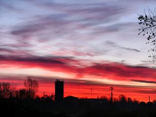 Fiery red sky illuminating industrial silhouettes at dawn