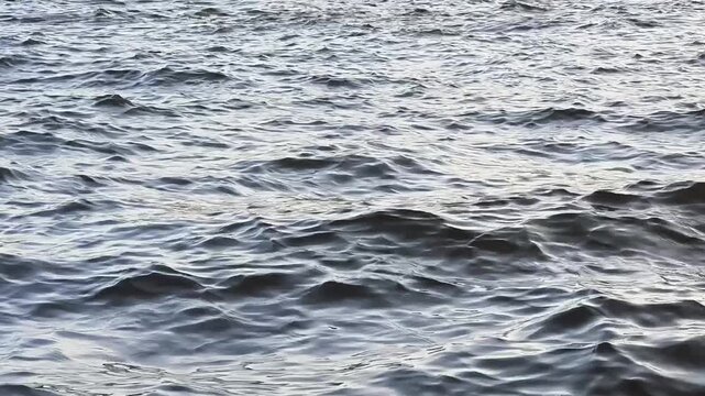 Choppy silver waves on river with reflection under cloudy sky. Кestless and dynamic mood, a bit of confusion and turmoil. Abstract nature pattern, natural water texture, water waves texture.