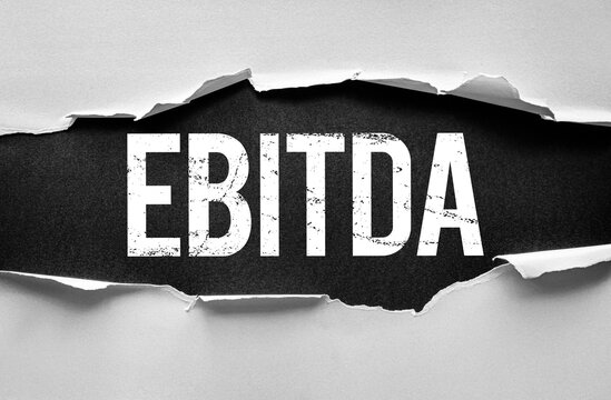 EBITDA text in distressed bold typography under torn paper. Financial and business concept image referring to earnings before interest, taxes, depreciation, and amortization for analysis