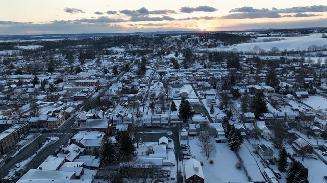 Peaceful winter sunset over snow covered American town. Aerial view of quiet residential neighborhoods, soft evening light, calm atmosphere and snowy rooftops stretching toward horizon. Wide shot.