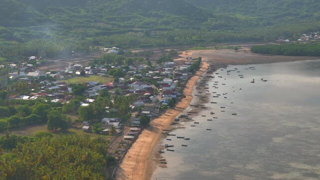 Aerial drone view of coastal village with sandy beach fishing boats calm sea tropical hills shoreline cinematic travel landscape suits tourism coastal lifestyle island scenery and nature exploration