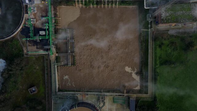 Drone flight over sugar production clarification tanks and cooling lagoons showing sediment and brown liquid in large industrial basins UK