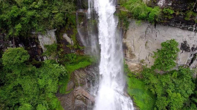 Close aerial pullback across Ramboda waterfall flow surrounded by dense green forest in Nuwara Eliya Sri Lanka