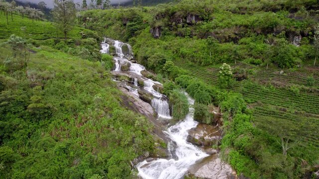 Long Ramboda waterfall winds across green valley hills and forest in Nuwara Eliya Sri Lanka, aerial panoramic pullback