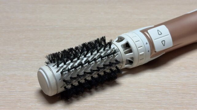 The rotating brush head of this hair styler spins smoothly against the hair. This mechanical action produces a rhythmic, low-pitched hum and a soft whirring sound of rushing air.