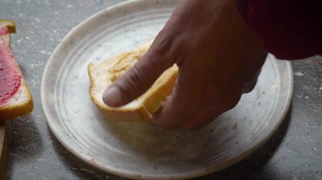 Making a Classic Peanut Butter and Jelly Sandwich man 's hands apply jam on a slice of toasted bread with peanut butter cream close - up. home cooking breakfast 4K video