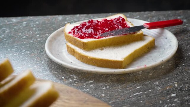 Spreading Red Jam on a Slightly Browned Toast with Table Knife on Cutting Board. A man spreading jam over a White bread slice 4k Video