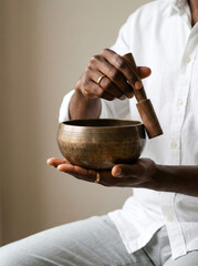 Man plays singing bowl with mallet for sound therapy in bright room