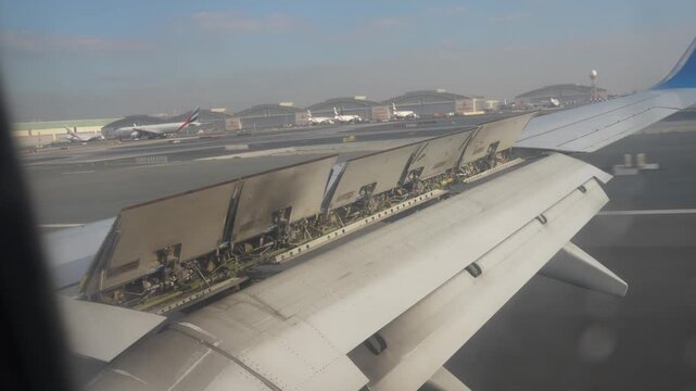 Abu Dhabi, UAE - January 18, 2026: Aircraft wing with extended flaps is shown from a window view, approaching the runway at an airport, with various planes and hangars visible in the background