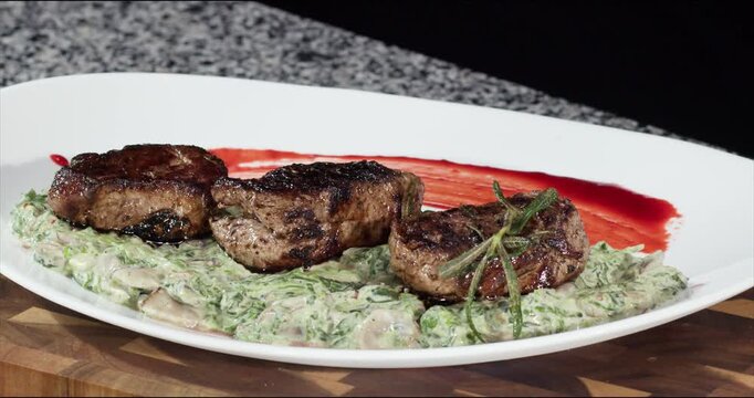 Decorating beef steaks with fried rosemary twigs on grey table closeup. Presentation of luxury meat dish with seasoning in restaurant. Nutritious food