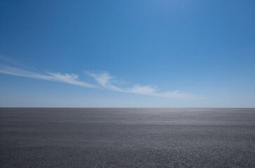 Fototapeta premium Open Asphalt Space Under a Vibrant Blue Sky with Wispy Clouds, Ideal for Commercial Mockups