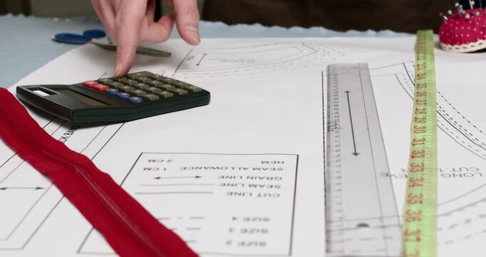 Man tailor checks measurements and enters digits into calculator. Male precisely places ruler on pattern and makes numerical calculations on calculator