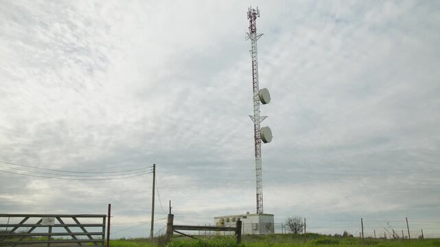Low-angle view of a steel lattice telecommunication mast featuring large white microwave drum antennas and a base station equipment shelter