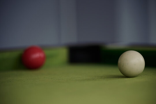 Low view of a white cue ball on a pool table and corner pocket and red ball in blurred background