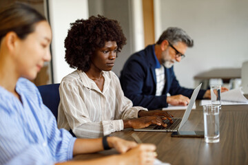 Fototapeta premium Focused businesswoman typing on laptop and analyzing data while working with colleagues in modern office