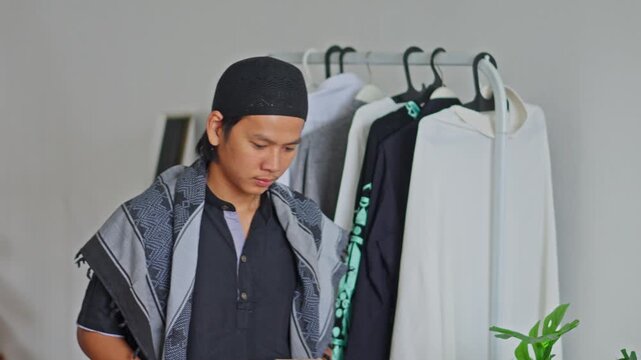 Smiling Muslim man holding cardboard box in front of clothes rack
