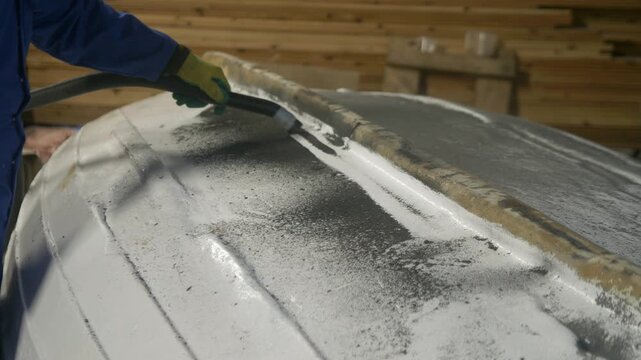 Vacuuming sanded depris from upturned boat hull in workshop