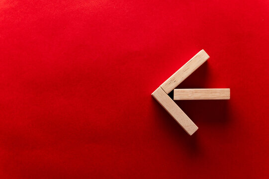 Wooden blocks arranged in a left arrow shape on a vibrant red background, showcasing geometric design and minimalistic style for creative projects From right to left