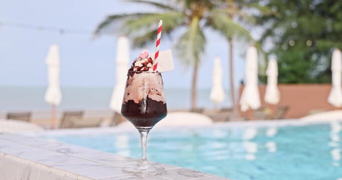 Chocolate frappe with whipped cream and heart candy standing poolside at a luxurious tropical resort with a sparkling blue swimming pool, palm trees, and ocean view. Luxury vacation, summer resort