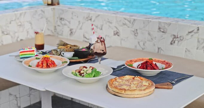 Luxurious poolside dining table displaying a vibrant spread of gourmet dishes and refreshing cocktails, with a sparkling blue swimming pool in the background. A concept of summer vacation, resort