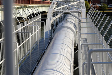 Fototapeta premium Large White Water Supply Pipe Bridge Crossing a River in an Urban Area. Essential Public Infrastructure for Water Management, Engineering, and Utility Services in Japan.