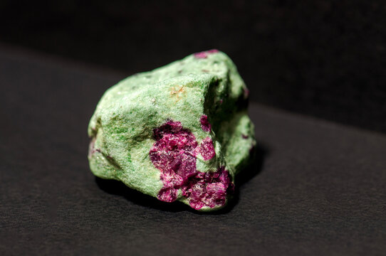 Raw ruby in zoisite mineral stone on a dark background. Natural green zoisite matrix with vibrant pink ruby crystals, macro close-up with detailed texture. Geological specimen and collectible mineral 