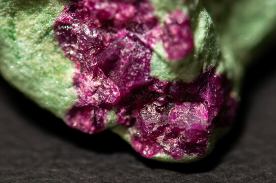 Raw ruby in zoisite mineral stone on a dark background. Natural green zoisite matrix with vibrant pink ruby crystals, macro close-up with detailed texture. Geological specimen and collectible mineral 