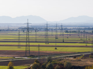 High-voltage transmission towers and power lines run through fields and hills showing the energy...